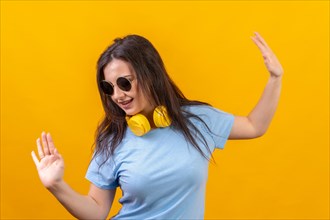 Studio portrait with yellow background of a woman with sunglasses dancing with headphones on lying