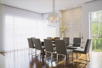 Glass dining table with gray upholstered high back chairs in dining room inside luxurious home,