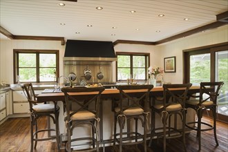 Country style kitchen with island and rustic wooden high chairs inside New Hampton style home,