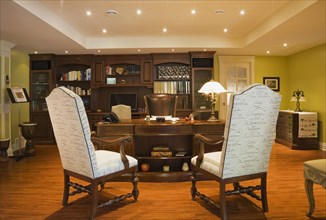 Wooden desk, high back chairs and wall unit in basement home office inside elegant style home,