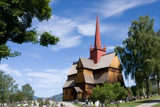 A traditional Norwegian stave church with a red roof under a clear blue sky surrounded by a