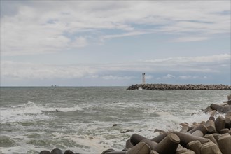 Waves crash against the breakwater with a lighthouse in the distance under a gray sky, in Ulsan,