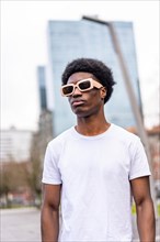 Vertical portrait of a modern african young man in sunglasses and casual clothes int he city