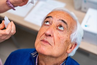 Close-up top view of a senior man looking up while ophthalmologist applying drops in the eyes in a