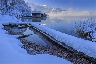 Morning atmosphere at mountain lake in front of mountains, boat huts, shore, winter, snow,