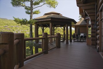 Brown stained gazebo on wooden deck with tempered glass and log railings attached to back of