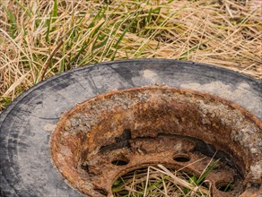 Close-up of a rusty tire rim surrounded by dry grass, in South Korea