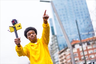 African young vlogger pointing ahead during an online video with a mobile attached on mic and