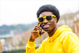 Stylish smiling african man looking at camera while using phone in the city