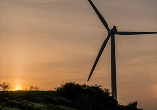 Wind turbine silhouette against cloudy sky as sun sets behind mountain top in South Korea