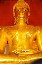 Golden Buddha statue in a serene meditation pose against a red backdrop