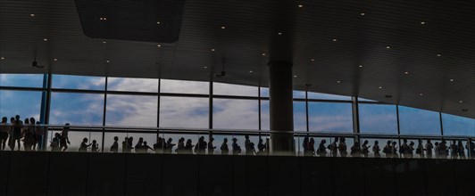 Silhouette of people standing in line on upper floor of airport building in front of blue sky