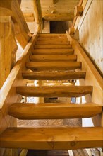 Wooden log stairs leading to upstairs floor inside handcrafted red cedar log cabin home, Quebec,