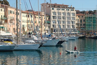 Sailing boats moored in a quiet harbour in front of colourful buildings under a clear blue sky Elba