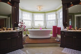 Master bedroom en suite with freestanding white bathtub on raised platform and his and her vanities