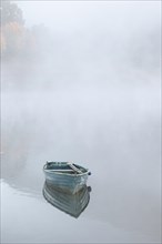 Wooden boat floating in the water, surrounded by fog, in the background barely recognisable