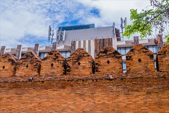 Ancient style brick wall with modern structures and cell towers behind, in Chiang Mai, Thailand,