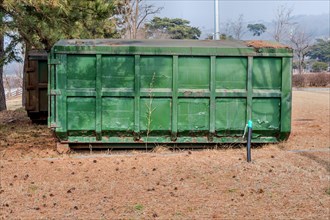 An old green dumpster sits in a field of dry grass, in South Korea