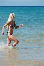 A blonde woman in a bikini enjoys walking in the shallow water at the beach on a sunny day