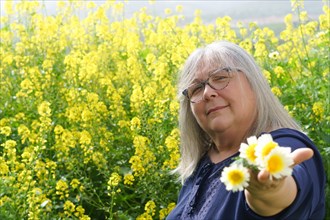 Older woman in the countryside holding beautiful wild daisies in her hands