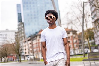 Confident cool and young african man in white clothes and sunglasses walking along the city