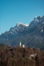 St. Niklaus Church in front of the snow-covered Zahmer Kaiser, surrounded by forest under a clear