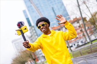 Cool african young content creator waving at camera steaming live standing in a city
