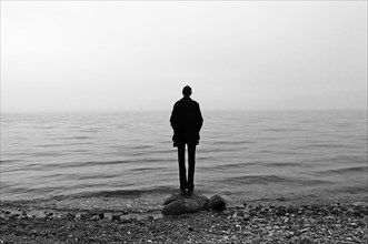 Young man stands on the beach in cloudy weather and looks at the Baltic Sea, Gross Schwansee,