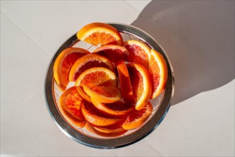 A glass bowl full of fresh orange slices in the sunlight, from above