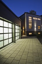 Illuminated two car garage and beige stone with brown cedar wood siding modern cubist style home