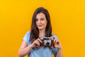 Studio portrait with yellow background of a woman holding a retro photographic camera on hands