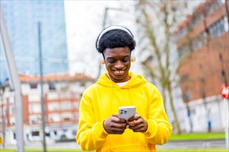 Cool and happy african young man listening to music using mobile in the city