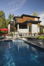 Two story grey, beige and tan cut stone with wood siding and black trim home and inground swimming