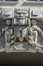Decorative figures above gateway in Art Nouveau style, naked boys with garland, grim male face,