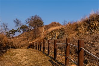 Rope fence next to hiking trail to wooden stairway up side of mountain under blue sky in Boeun,