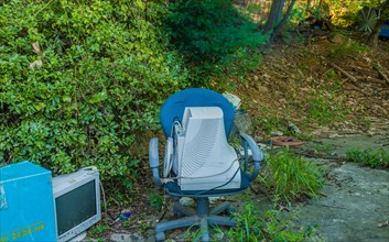 Old CRT computer monitors discarded in rural wooded area. One in old chair the other on the ground