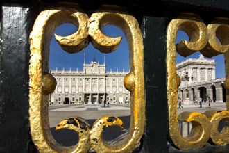 View of a historic royal palace through a gold-decorated wrought-iron gate, blue sky with clouds in