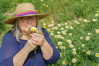 Mature woman with white hair and hat with a bouquet of daisies in her hands, in the background a
