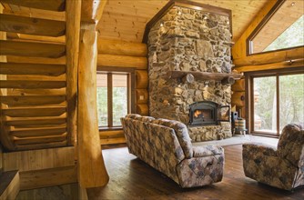 Wooden log stairs and upholstered sofas with lit fieldstone and porous rock fireplace in living