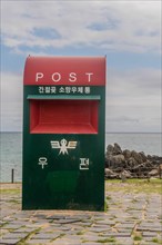 Close-up of a red and green mailbox with Korean text against a sea backdrop, in Ulsan, South Korea,