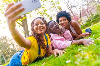 Three african female friends taking a selfie lying on urban park