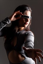 Studio portrait with grey background of a sensual futuristic woman using virtual reality goggles