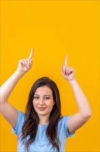 Studio portrait with yellow background of a caucasian casual woman pointing up to a blank space