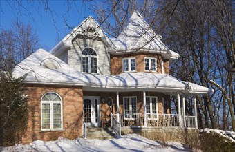 Two story red brick Victorian style home with white trim and landscaped front yard in winter,