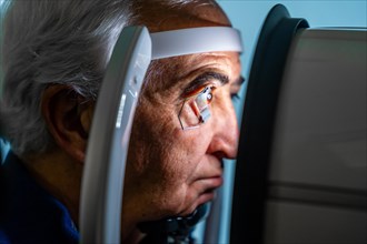 Close-up photo of a serious senior man with eye opener looking through an innovative machine during