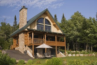 Handcrafted two story spruce log home cabin with fieldstone chimney and green sheet metal roof in