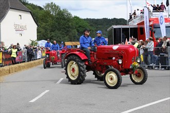 Porsche diesel tractors, drivers in blue present their red vintage tractors at a street festival,