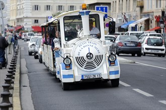 Marseille, A tourist train with passengers travelling through a busy city street, Marseille,