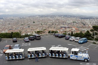 Marseille, A viewpoint with parked cars and tourist trains overlooks a large city, Marseille,