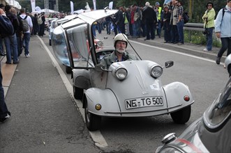 Small white car with a driver in a helmet, spectators line the road, SOLITUDE REVIVAL 2011,